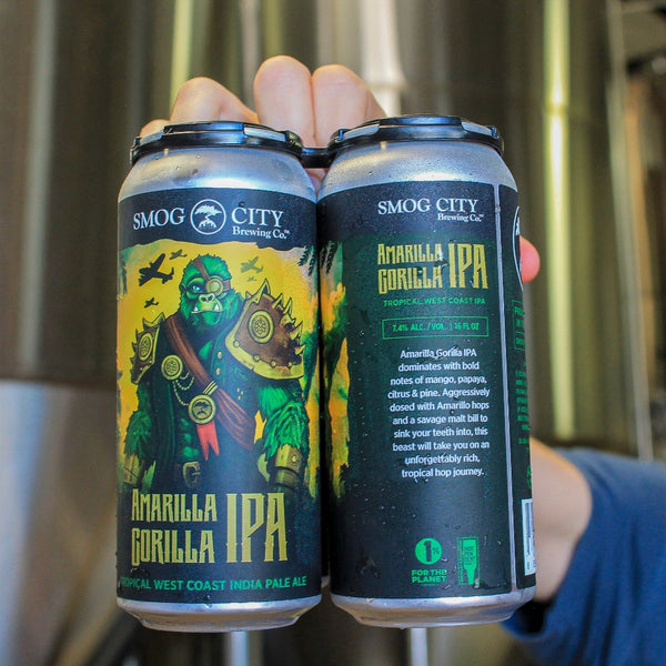 hand holding a 4-pack of Amarilla Gorilla in front of stainless steel fermenting tanks