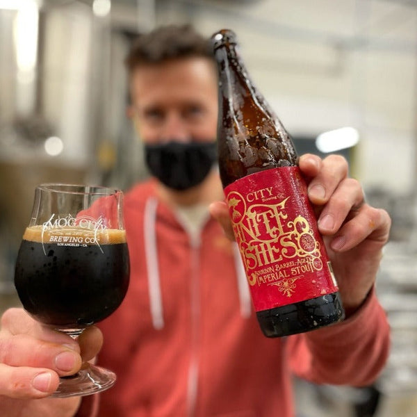 Man holding a bottle of beer and a glass of dark beer toward the camera.