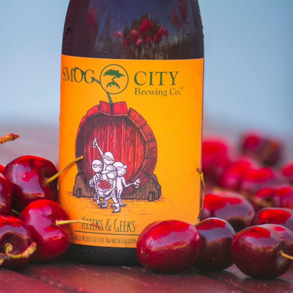Bottle of Krieks & Geeks with label art surrounded by a pile of cherries