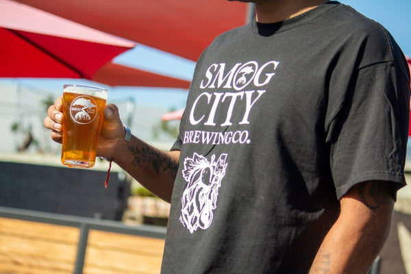 Man's torso with black Smog City IPA Hop T Shirt holding a beer in his hand.